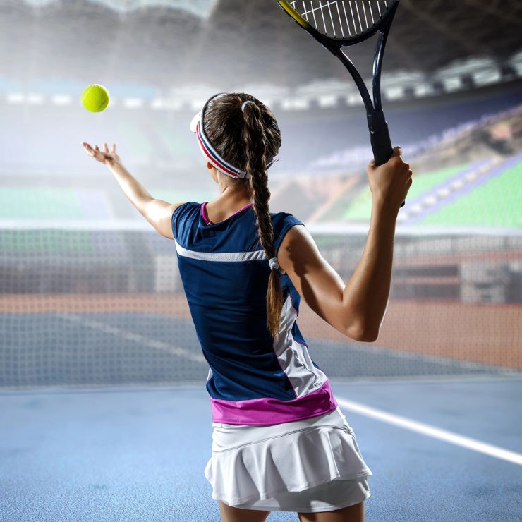 A focused female tennis player preparing to serve during a match, captured in mid-motion with her racket raised and the ball in the air. This dynamic image underscores the benefits of LED light therapy offered by Genesis Sports Therapy, of Hickory, NC, which helps increase athletes' endurance. The player's poised and powerful stance highlights the enhanced performance and stamina achieved through specialized therapy.