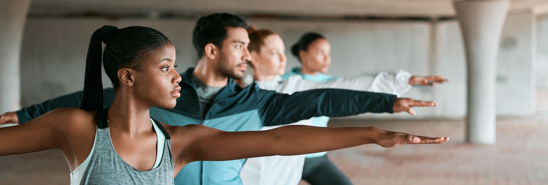 A diverse group of focused individuals practicing yoga or stretching exercises, extending their arms in unison. The foreground features a woman with a ponytail, wearing a gray tank top, demonstrating strong posture and concentration. Genesis Sports Therapy specializes in the power of LED light therapy to help athletes achieve peak performance and swift recovery, assisting individuals like these to enhance their flexibility and strength. Let our dedicated, board-certified technicians show you the difference light therapy can make! Located at 231 13th Pl NW Suite B, Hickory, NC, 28601.