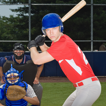 Baseball player in a red jersey and blue helmet preparing to bat, with a catcher in blue gear and an umpire behind him. Genesis Sports Therapy of Hickory, NC, offers LED light therapy to accelerate an athlete's recovery and enhance performance with targeted LED light therapy.