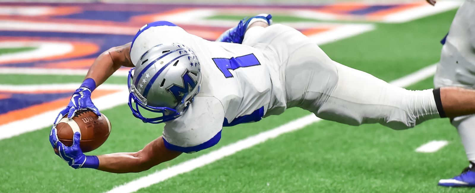 Football player in full gear makes a diving catch mid-air during a game, showcasing athletic performance at its peak. Genesis Sports Therapy, 231 13th Pl NW Suite B Hickory, NC, 28601, specializes in LED light therapy to help athletes like this recover swiftly and perform at their best.