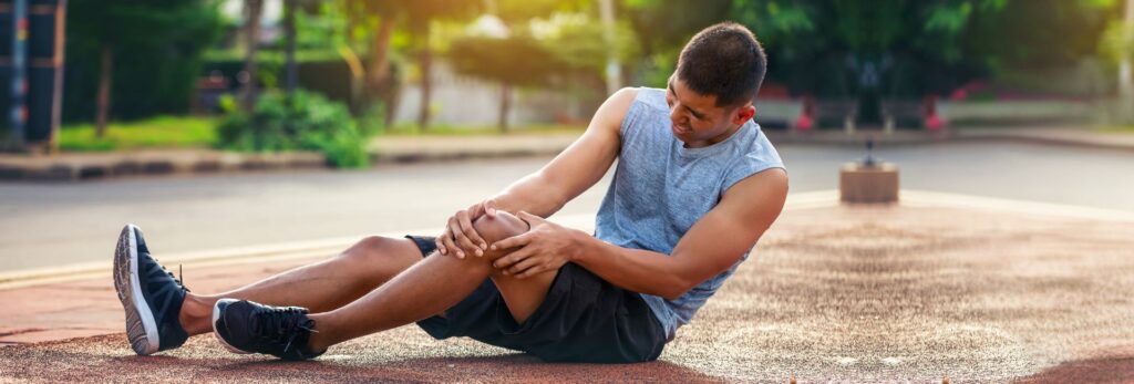 An athlete sitting on an outdoor track, clutching his knee in pain, demonstrating the physical toll of intense training. Genesis Sports Therapy in Hickory, NC, specializes in the power of LED light therapy to help athletes like this recover swiftly and achieve peak performance. Our board-certified technicians can show you the difference light therapy makes in rehabilitation and performance enhancement.