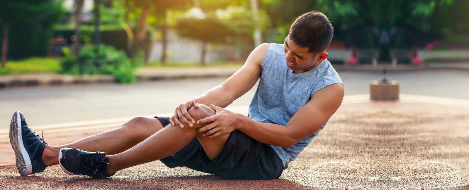 An athlete sitting on an outdoor track, clutching his knee in pain, demonstrating the physical toll of intense training. Genesis Sports Therapy in Hickory, NC, specializes in the power of LED light therapy to help athletes like this recover swiftly and achieve peak performance. Our board-certified technicians can show you the difference light therapy makes in rehabilitation and performance enhancement.