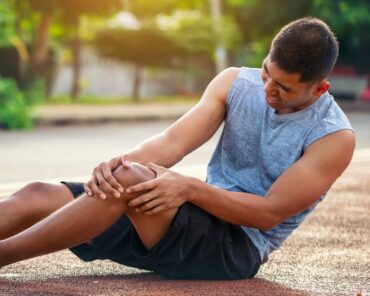 An athlete sitting on an outdoor track, clutching his knee in pain, demonstrating the physical toll of intense training. Genesis Sports Therapy in Hickory, NC, specializes in the power of LED light therapy to help athletes like this recover swiftly and achieve peak performance. Our board-certified technicians can show you the difference light therapy makes in rehabilitation and performance enhancement.
